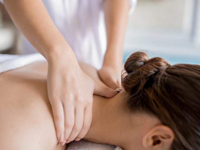 Hands of masseuse massaging neck and shoulders of relaxed client in spa salon
